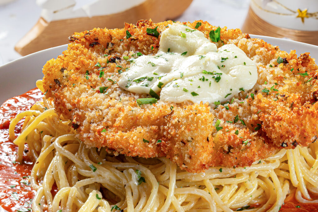 Golden, crispy breaded chicken Parmesan topped with melted mozzarella cheese, served over creamy spaghetti Alfredo with a rich marinara sauce, garnished with fresh parsley, from Brio Italian Grille.