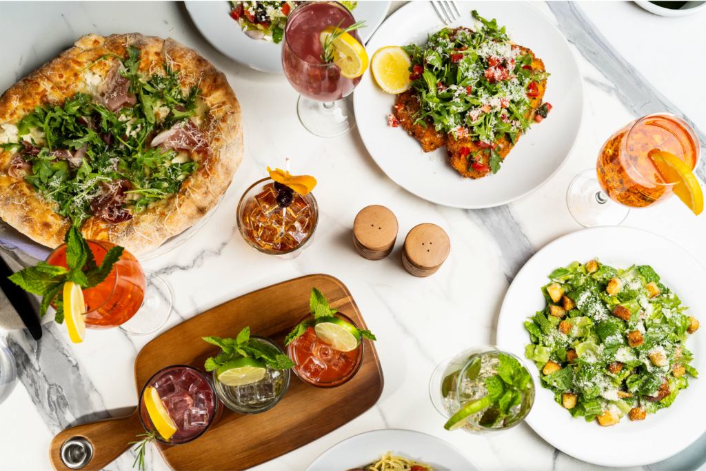 Table spread with pizza, salads, cocktails and summer dishes.